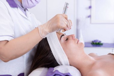 Güzellik uzmanı güzellik salonundaki genç bayan müşterinin yüzüne yüz bakımı uyguluyor. Kozmetoloji ve profesyonel cilt bakımı..