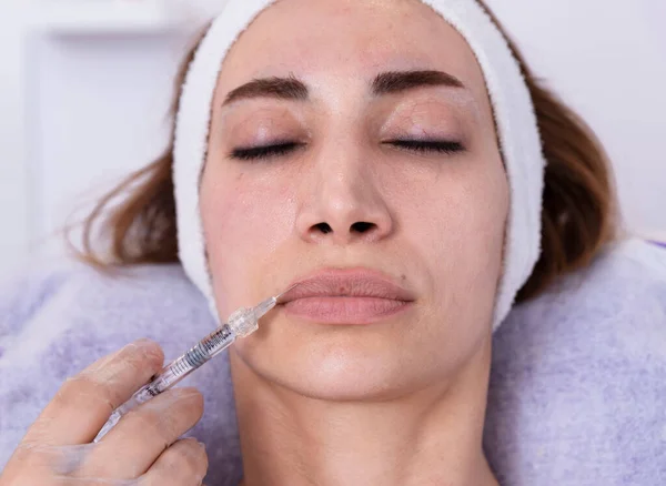 Cosmetologist performs lip filler injections with hyaluronic acid filler in a woman\'s face Cosmetology female aesthetic in a beauty salon, lip augmentation procedure