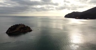 Okyanustaki küçük yalnız bir ada, dağ siluetinin üzerinde batan gökyüzü güneşi. Tropikal ve hiç kimse. Plaj alanı arka planı. Portekiz, Algarve bölgesi. Faro. Küçük ve sakin dalgalar. Metin uzayı. 