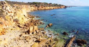 Kayalık sahil şeridinin üzerinde kamera uçuyor. Sahildeki kayalık doğa arka planı. Algarve plajında turizm gezisi. Vahşi doğanın sinematik hava manzarası. Sakin dalgalar yavaşça sahile çarpıyor.