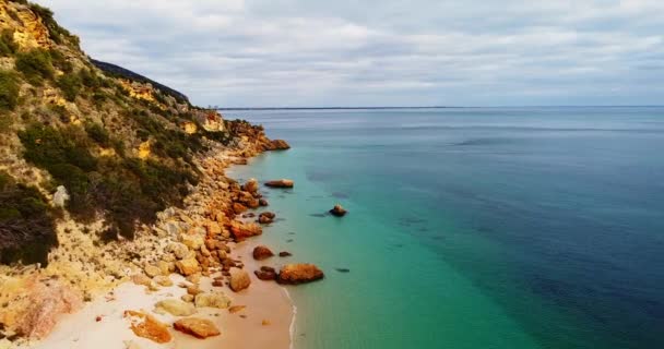 Kayalık sahil şeridinin üzerinde kamera uçuyor. Sahildeki kayalık doğa arka planı. Algarve plajında turizm gezisi. Vahşi doğanın sinematik hava manzarası. Sakin dalgalar yavaşça sahile çarpıyor. — Stok video