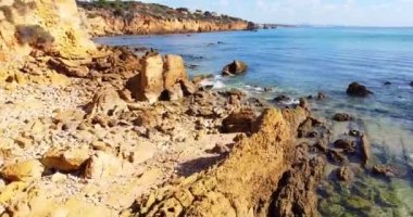 Kayalık sahil şeridinin üzerinde uçmak ve kamerayı okyanusa doğru eğmek. Doğrudan güneşe uçuyor. Altın kayalara ve derin mavi kristal berrak suya yakın uçuyor. Doku ve seyahat kavramı. 