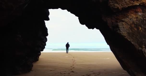A guy is walking out of the cave to look at the ocean. Atlantic ocean, big waves — Stock Video