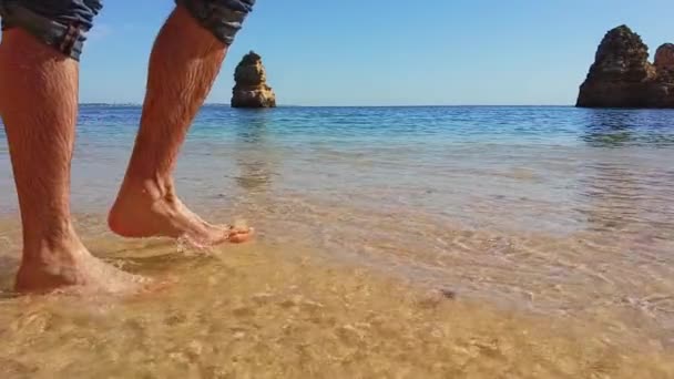 Zbliżenie na stopy mężczyzny spacerującego po plaży. Fale powoli się poruszają i usuwają ślady stóp. Męskie nogi, stopa. Chodzenie po złotym białym piasku i odbiciu. Przejrzysta woda poruszająca się swobodnie — Wideo stockowe