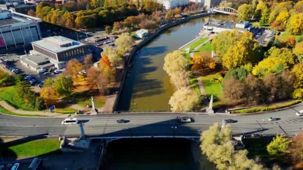 カラフルな秋の街 下の川の上を飛ぶ 橋を渡って車に乗る 交通路だ 太陽の木に輝く 市内の黄金の時間の日没 エストニアだ 川の横を歩く人々 — ストック動画