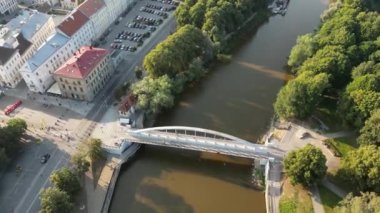 Şehir manzarası. Eski kasaba manzarası. İnsansız hava aracı insanların yaz günbatımında köprüden geçişlerini gösteriyor. İnsansız hava aracıyla uzaklaşıyorum. Yeşil şehir. Estonya, Tartu. Kırmızı çatıdaki binalar. Ortaçağ 