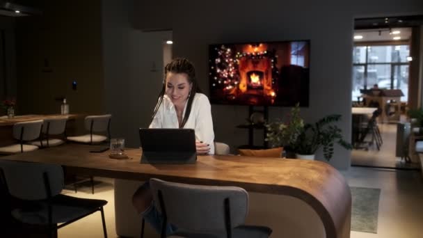 Una hermosa joven con rastas se sienta en una mesa con una tableta y se comunica a través de un enlace de vídeo con su familia. Concepto de comunicación. — Vídeo de stock