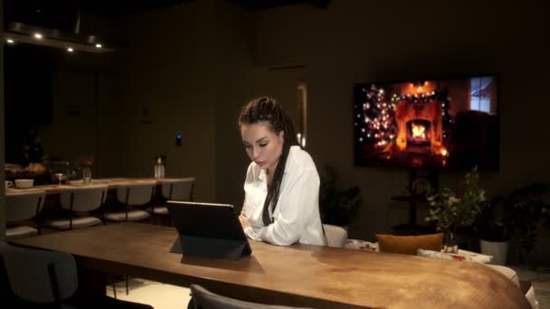 Uma menina com dreadlocks em uma camisa branca está estudando artigos em um tablet para seu trabalho. Conceito de aprendizagem online. — Vídeo de Stock