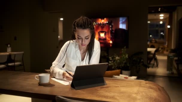 En flicka med dreadlocks i en vit skjorta med hjälp av en digital surfplatta på en online lektion, lär sig av video via en surfplatta. Begreppet lärande online. — Stockvideo