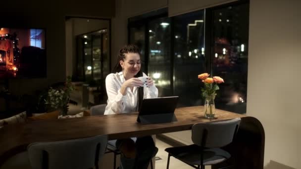 Una bella ragazza con i dreadlock siede a un tavolo con un tablet e comunica tramite collegamento video con la sua famiglia. Concetto di comunicazione. — Video Stock