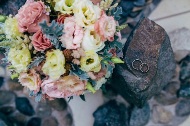Gelin buketi ve taşın üstünde alyanslar.