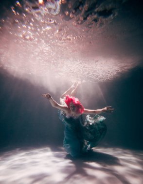 Suyun altında çok güzel bir elbiseyle çekim yapan genç bir kadın.