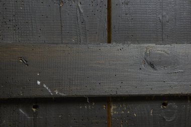 Eski tahtalar solucanlar tarafından hasar görmüş, yakından görülmüş, kapılar siyaha boyanmış, kalaslar birleşmiş.