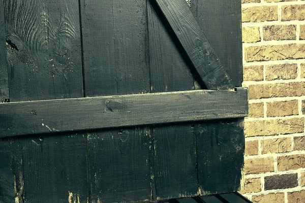 Eski tahtalar solucanlar tarafından hasar görmüş, yakından görülmüş, kapılar siyaha boyanmış, kalaslar birleşmiş.