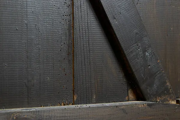 Eski tahtalar solucanlar tarafından hasar görmüş, yakından görülmüş, kapılar siyaha boyanmış, kalaslar birleşmiş.