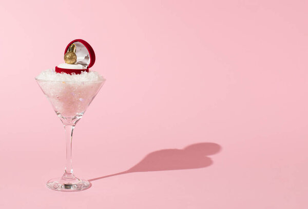 Коктейльный бокал со снегом и красным кольцом подарочная коробка с золотым рождественским шаром на розовом фоне. Творческая концепция новогоднего праздника. Романтика или юбилей.