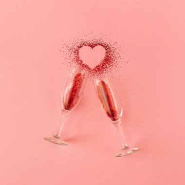 İki şampanya kadehinden yapılmış yaratıcı bir aşk fikri ve pastel pembe arka plan şeklinde parlak kırmızı bir kalp. Minimum Sevgililer Günü veya romantik bir konsept. Üst manzara, düz uzanma.