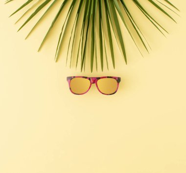 Pastel sarısı arka planda palmiye yaprağı ve güneş gözlüğü. Minimum yaz seyahati ya da tropik tatil konsepti. Boşluğu kopyala.