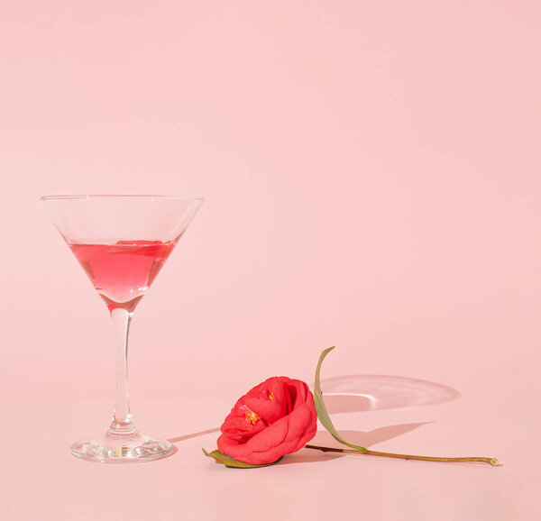 Martini glass and camellia flower on pink pastel background. Minimal party concept. Wedding day or love concept. Top view, copy space.