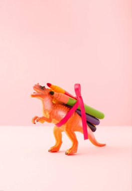 Dinosaur with crayons on pastel pink background. Minima back to school or fun creativity concept.