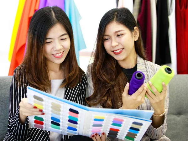 两个穿着商务服装的女人一起坐在服装店里 观察并比较样品目录中的线的颜色 裁缝店工作及集思广益的概念 — 图库照片