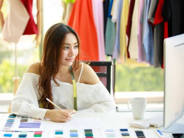 A beautiful young designer with a cheerful personality is smiling with joyful hands posing in her office in a designer clothing store. Business owner and start-up concept.