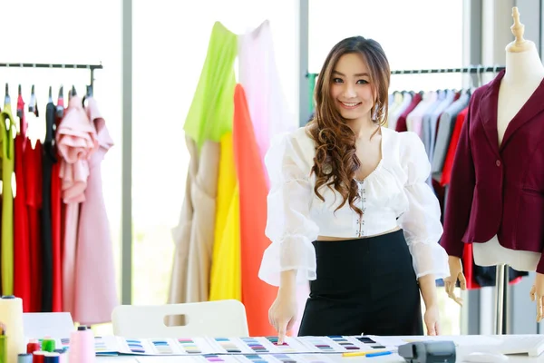 A beautiful young designer with a cheerful personality is smiling with joyful hands posing in her office in a designer clothing store.