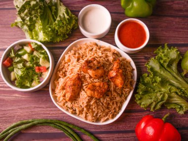 Hint ve Pakistanlı biryani anlaşmasının üst görüntüsü olan salata, raita, sos ve içecekle servis edilen bir tabakta tavuk tikka biryani.