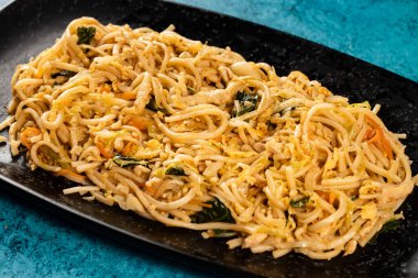 Baharatlı sebzeli Chow Mein siyah tepside mermer arka planda Çin yemeğinin üst görüntüsünde izole edilmiş.