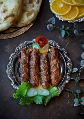 Koyu arkaplan görünümünde servis edilen yemekte servis edilen roti, salata ve limon dilimli Beef Seekh Kebap