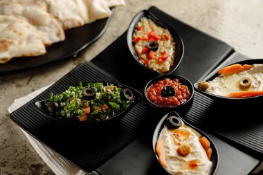 Karışık Mazzaa soslu kahvaltı Tabouleh Salatası, Humus ve ekmek. Gri arka planda izole edilmiş bir tabakta servis ediliyor.