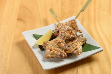 Japon yemeği Tebasaki 'yi ahşap masa manzarasında izole edilmiş beyaz bir tabakta kızarttı.