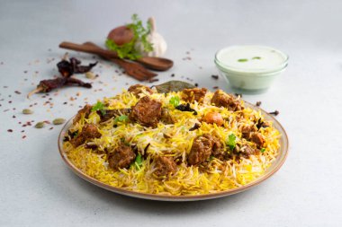 Hint baharatlı koyun eti biryani raita ve gulab jamun ile gri arka planda servis edilir.
