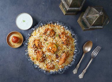 Hint baharatlı tavuk Tikka Biryani raita ve gulab jamun ile gri arka planda servis edilir.