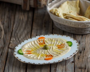 Humus, ahşap arka planda aperatif olarak izole edilmiş bir tabakta servis edilir.