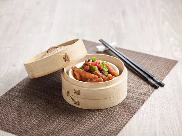 Steamed Chicken Claw with Black Bean Sauce served in a wooden bowl with chopsticks isolated on mat side view on grey marble background