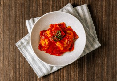 Lezzetli, domates soslu, peynirli ve fesleğenli Ravioli beyaz tabağın üstünde koyu ahşap masa manzaralı..