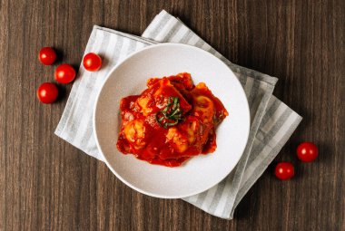 Lezzetli, domates soslu, peynirli ve fesleğenli Ravioli beyaz tabağın üstünde koyu ahşap masa manzaralı..