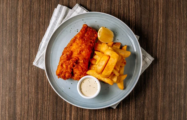 Traditional fried Fish and chips with tartar sauce in white plate on dark wooden background top view