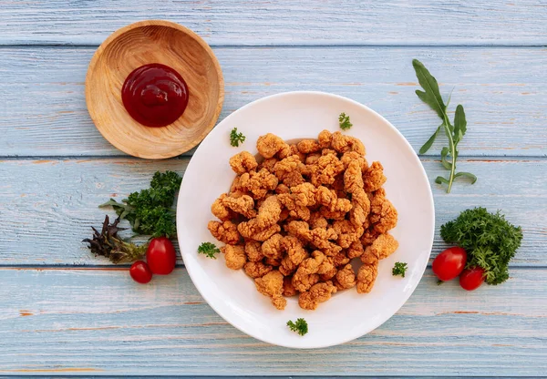 Homemade Crispy Popcorn Chicken in white plate with tomato ketchup and bbq sauce isolated on wooden table background top view fast food