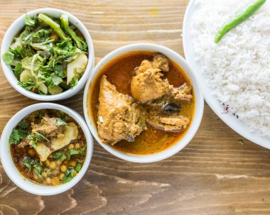chicken korma, dal chana, chicken curry, plain rice with onion, pepper and salad served in a dish isolated on wooden table top view of indian and bangladesh food