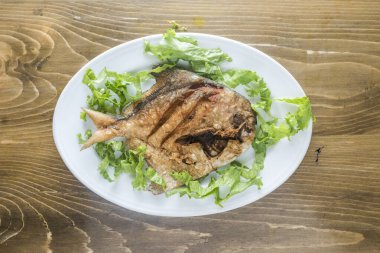 Pomfret Fried fish with onion, pepper and salad served in a dish isolated on wooden table top view of indian and bangladesh food