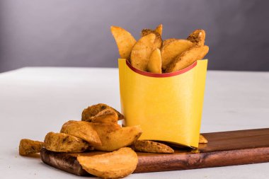 Crispy Potato wedges served in a basket isolated on wooden board side view of french fastfood