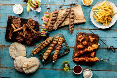 Arabic grills platter with kabab, seekh, tikka, boti, bread, pita, salad and fries isolated on cutting board side view of fastfood