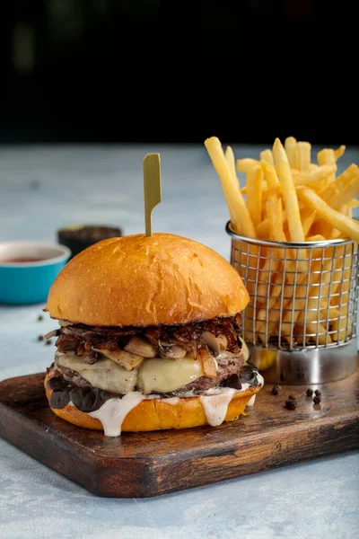 Juicy beef mushroom burger with dip and fries isolated on cutting board side view of fastfood