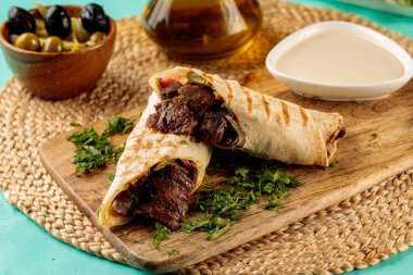 Et Saj Shawarma dürümü, mayonez soslu, ahşap masa başında, ortadoğu yemeği manzaralı tenha bir tabakta servis edilir.