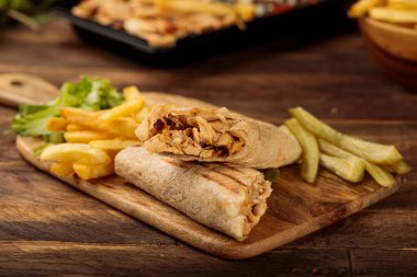 Tavuk sarmalı shawarma ve patates kızartması ahşap masa arkasındaki fast food manzarasında izole edilmiş bir kesme tahtasında servis ediliyor.