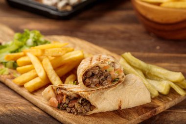Shawarma bifteği ve patates kızartması, ahşap masa arkasında izole edilmiş bir kesme tahtasında servis edilir.