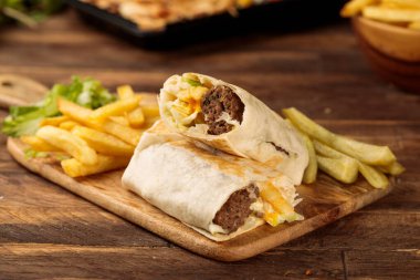 Biftek kebabı shawarma Wraps, ahşap masa arka planında izole edilmiş bir kesme tahtasına servis edilir.