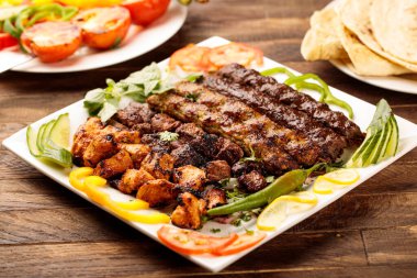 Tavuklu ızgara kebap, tikka, boti, salata ve ekmeği ahşap masa arkasında servis edilir.